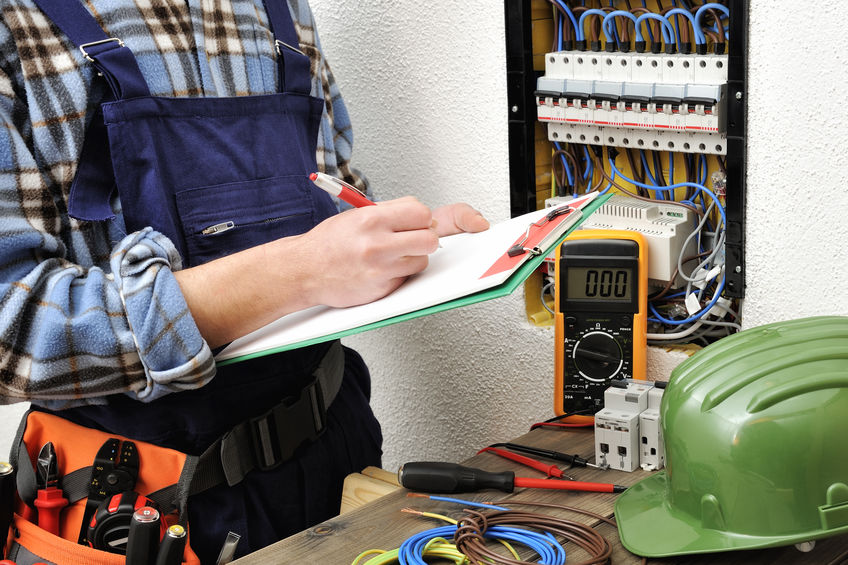 Young electrical technician writes in a notebook the data collected on a residential electric panel